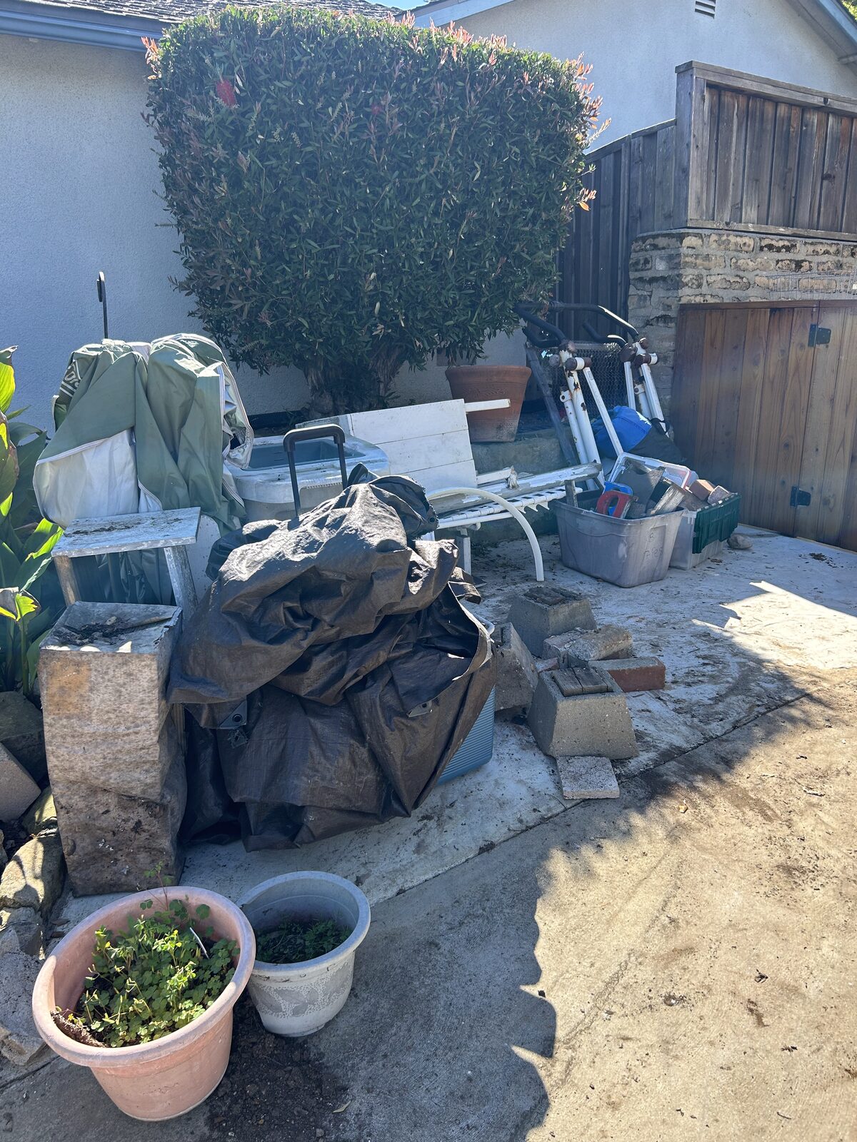 Before – backyard cluttered with tarps, bricks, and scooters in Santa Barbara